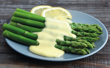 Green asparagus with sauce hollandaise and lemons on a plate, close-up