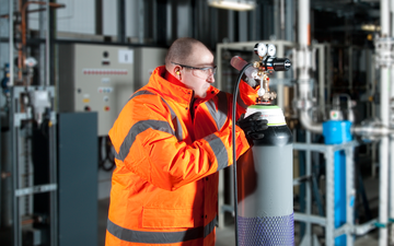An engineer wearing an orange high viz jacket inspecting an industrial gas cylinder