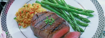 Filetsteak (medium fryed) on a plate decorated with green asparagus and rice. View on a table decoration.